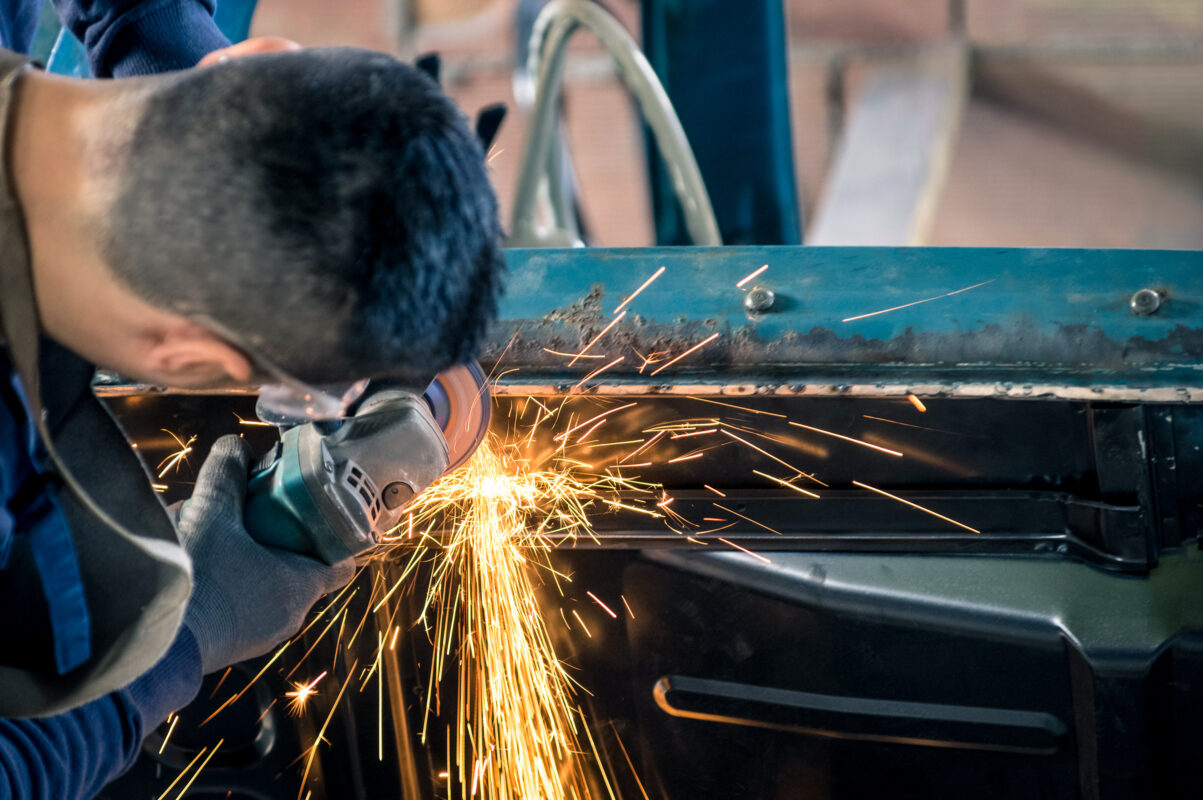 Young man mechanical worker repairing an old vintage car body in messy garage - Safety at work with protection wear